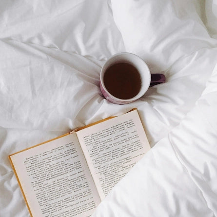 Open book and cup of tea on a white bedspread