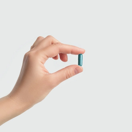 Hand holding a blue capsule against a light gray background