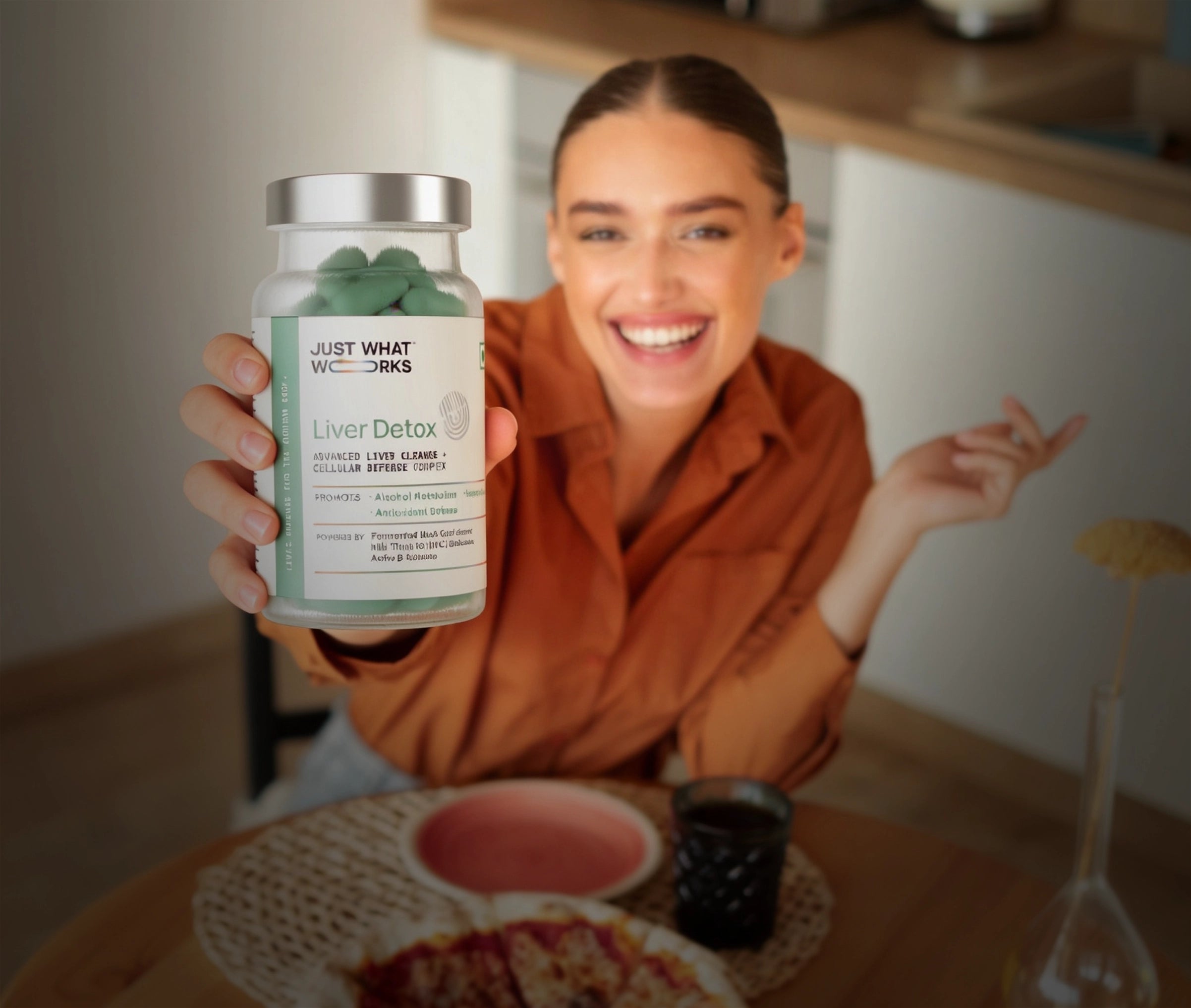 Woman holding a supplement bottle labeled 'Just What Works Liver Detox' in a kitchen setting.