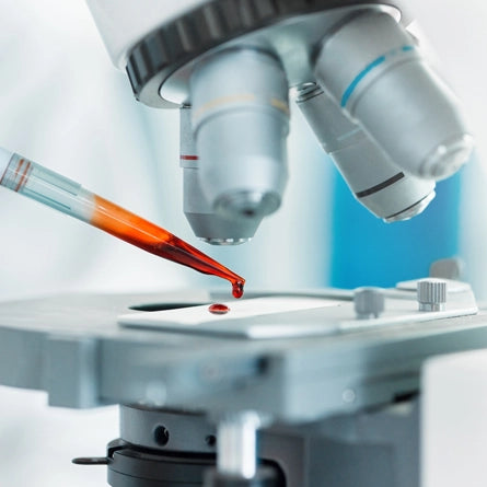Microscope with a red liquid sample being added to a slide