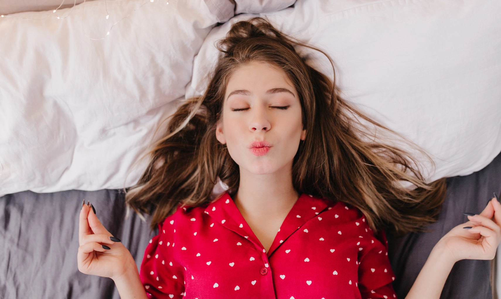 Woman in a red polka dot shirt lying on a bed blowing a kiss.