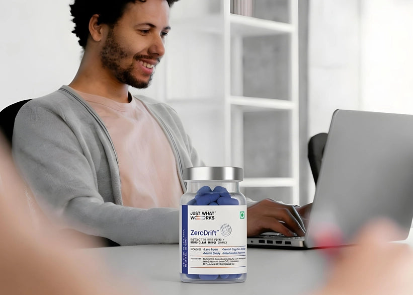 Person sitting at a desk with a laptop, holding a bottle labeled 'ZeroDrift'.