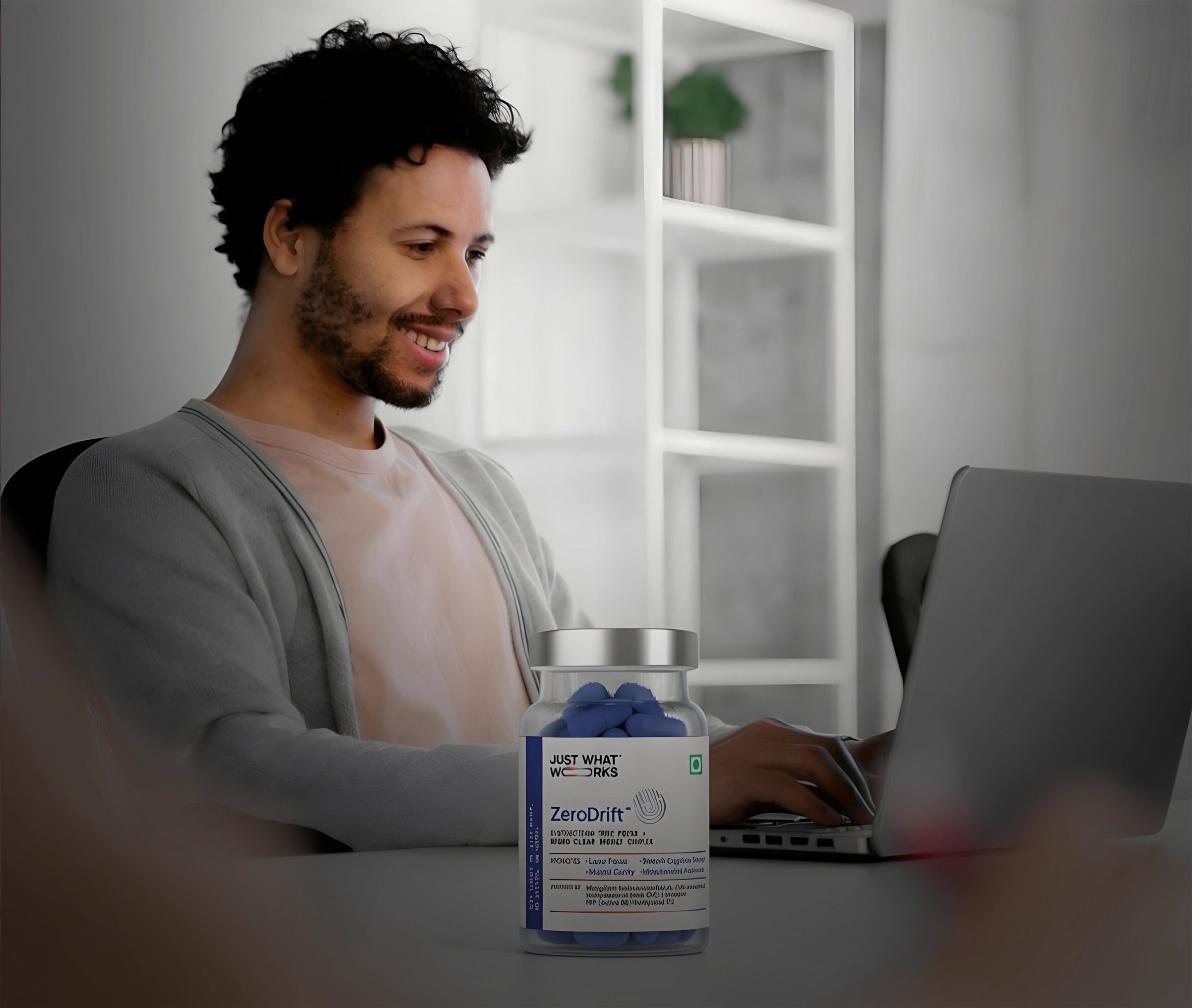 Man sitting at a desk with a laptop, looking at a jar of 'ZeroDrift' products.
